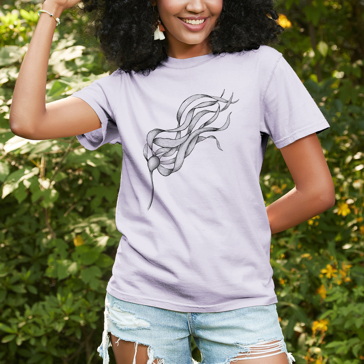 Woman wearing a Comfort Colors t-shirt printed with a black ink line drawing of a strand of bull kelp with long flowing blades, outdoors.