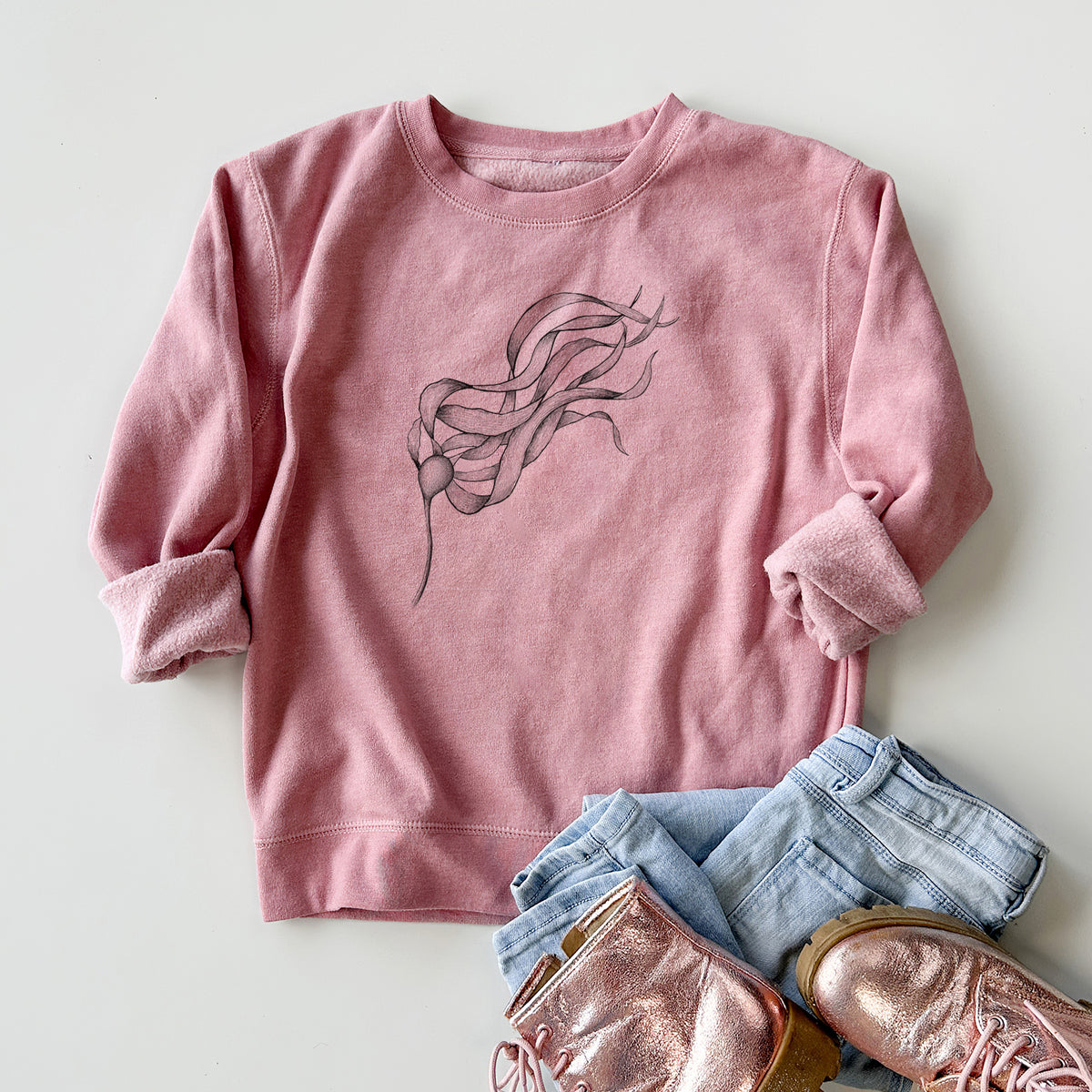 Youth crewneck sweatshirt printed with a black ink line drawing of a strand of bull kelp with long flowing blades, styled flat with jeans and boots.