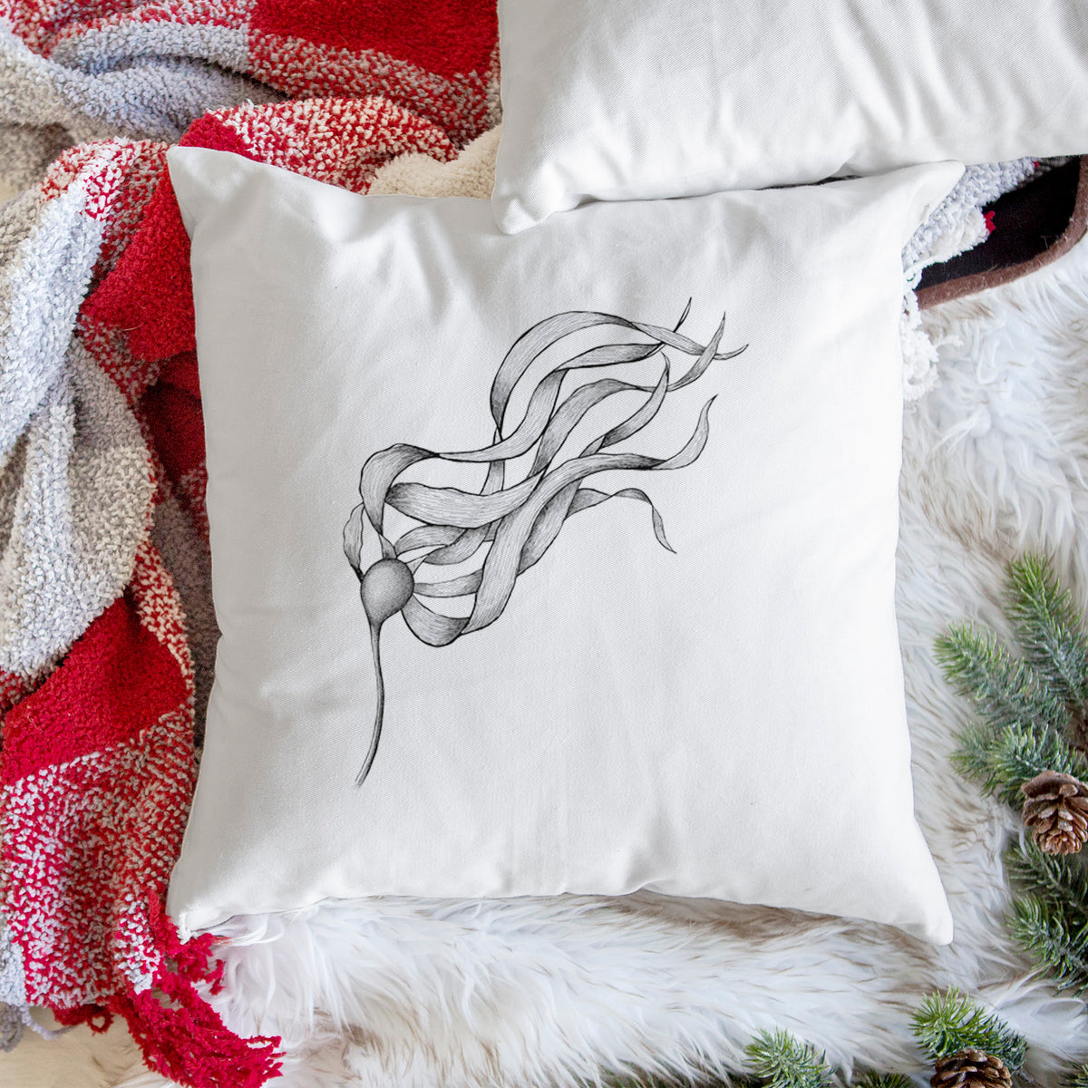 White pillow cover printed with a black ink line drawing of a strand of bull kelp with long flowing blades, on a woven chair.