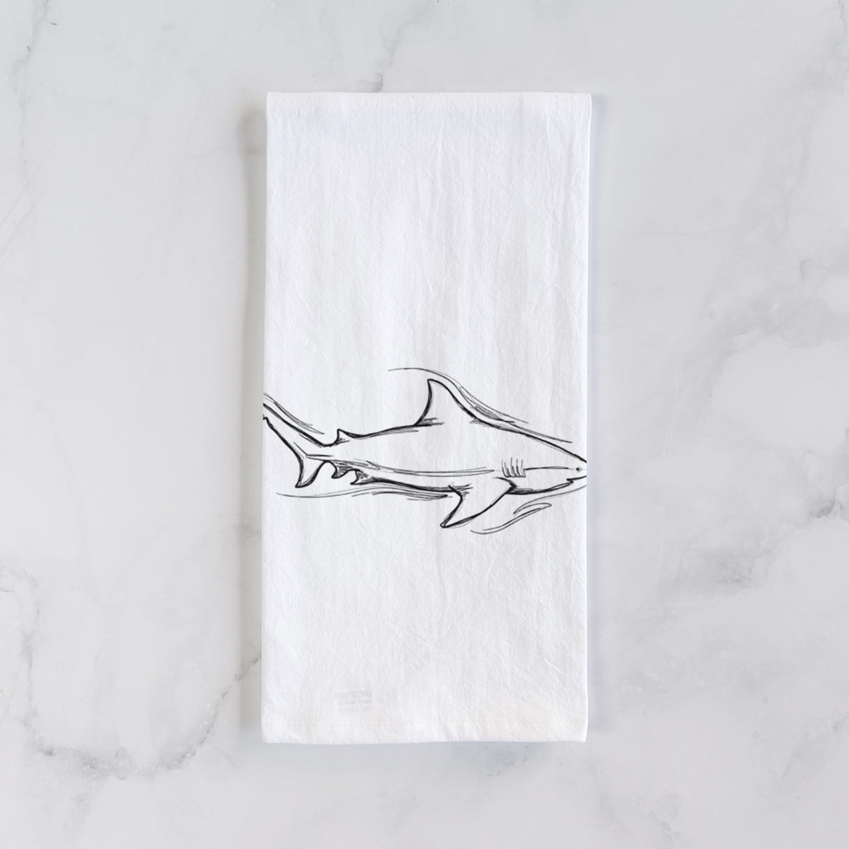 White cotton tea towel laid flat on marble, printed with a black ink illustration of a bull shark swimming.