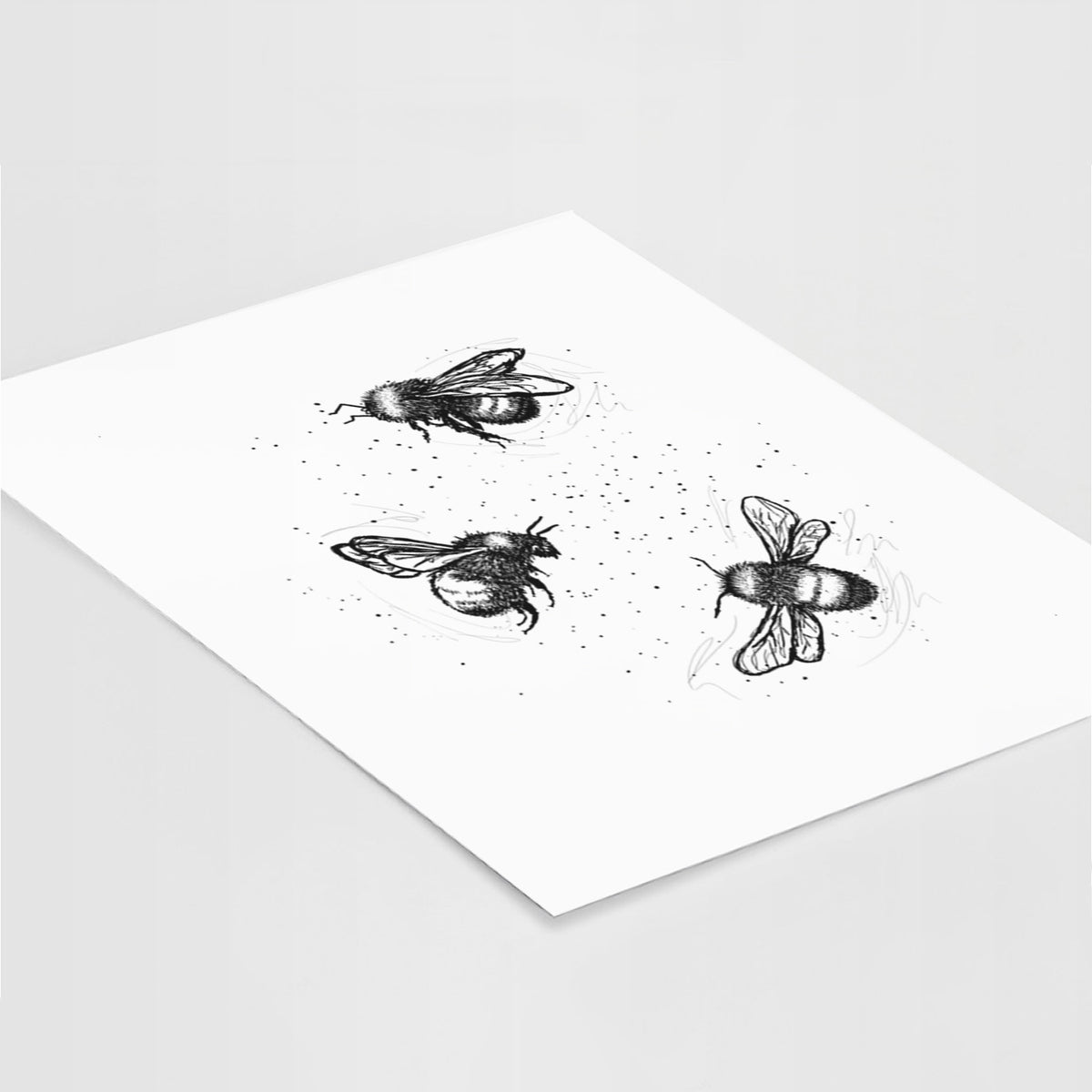 Art print of a black ink illustration of three bumble bees flying, lying at an angle on a white surface.