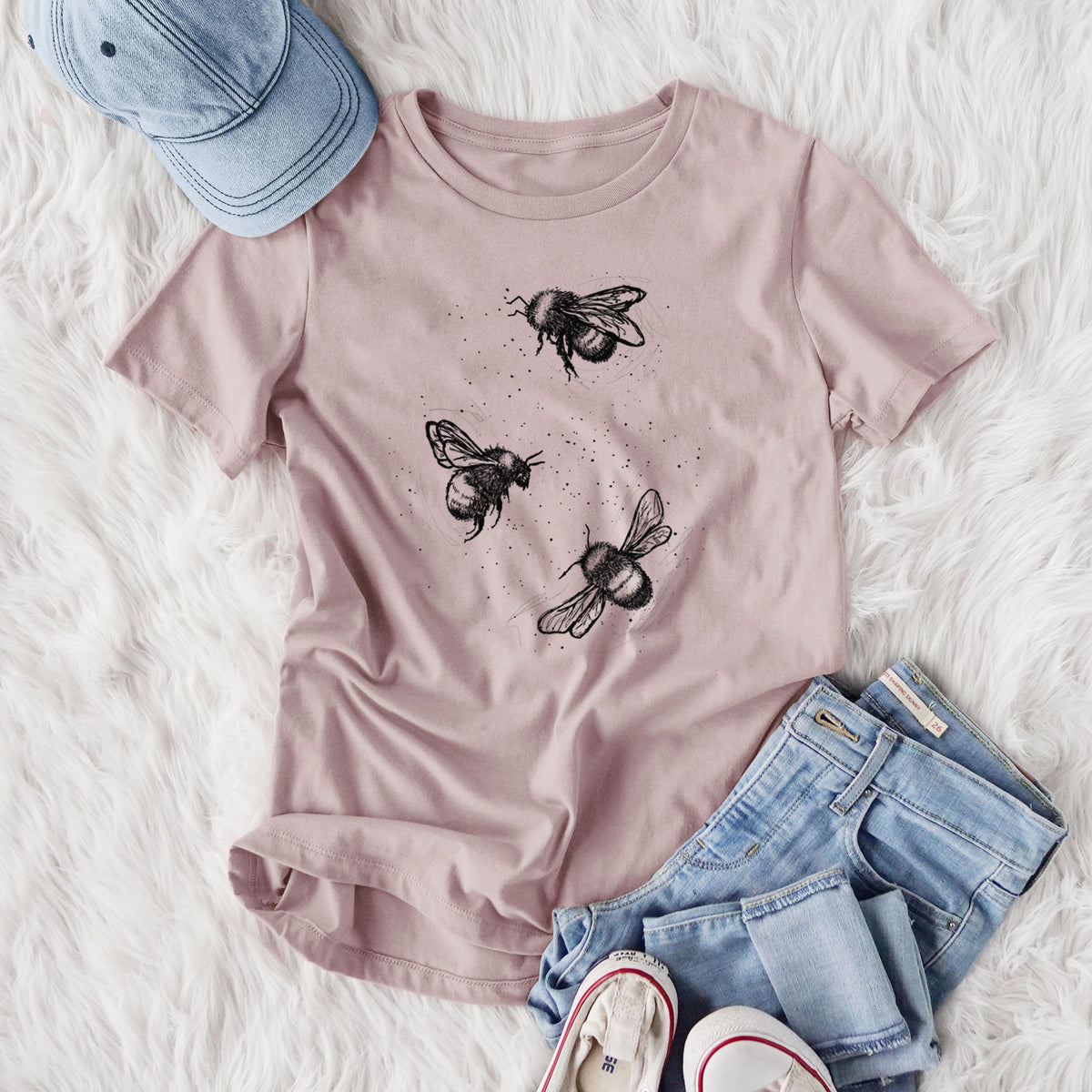 Women's relaxed fit cotton t-shirt printed with a black ink illustration of three bumble bees flying, styled flat on a white faux fur rug with jeans.