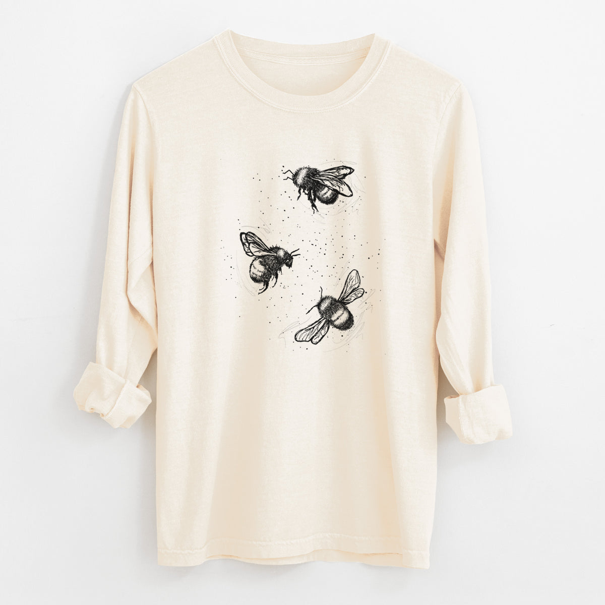 Ivory Comfort Colors long sleeve shirt laid flat with the cuffs rolled, printed with a black ink illustration of three bumble bees flying.