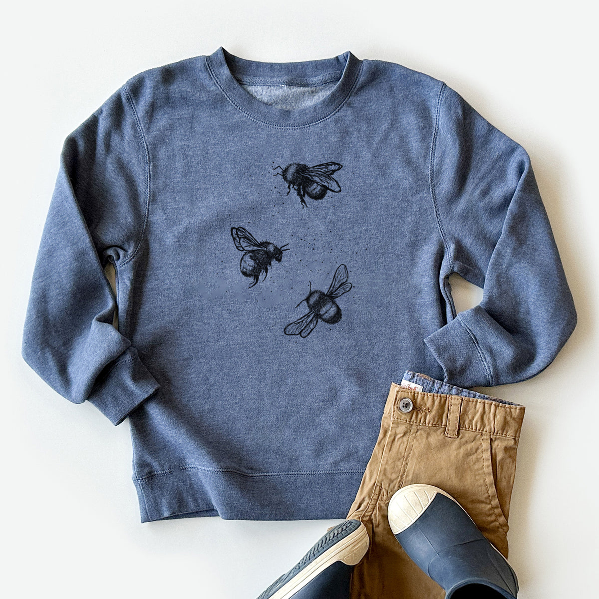 Youth crewneck sweatshirt printed with a black ink illustration of three bumble bees flying, styled flat with khaki pants and shoes.