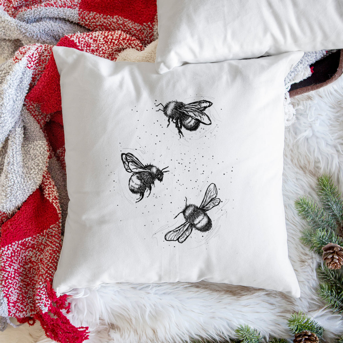 White pillow cover printed with a black ink illustration of three bumble bees flying, on a woven chair.