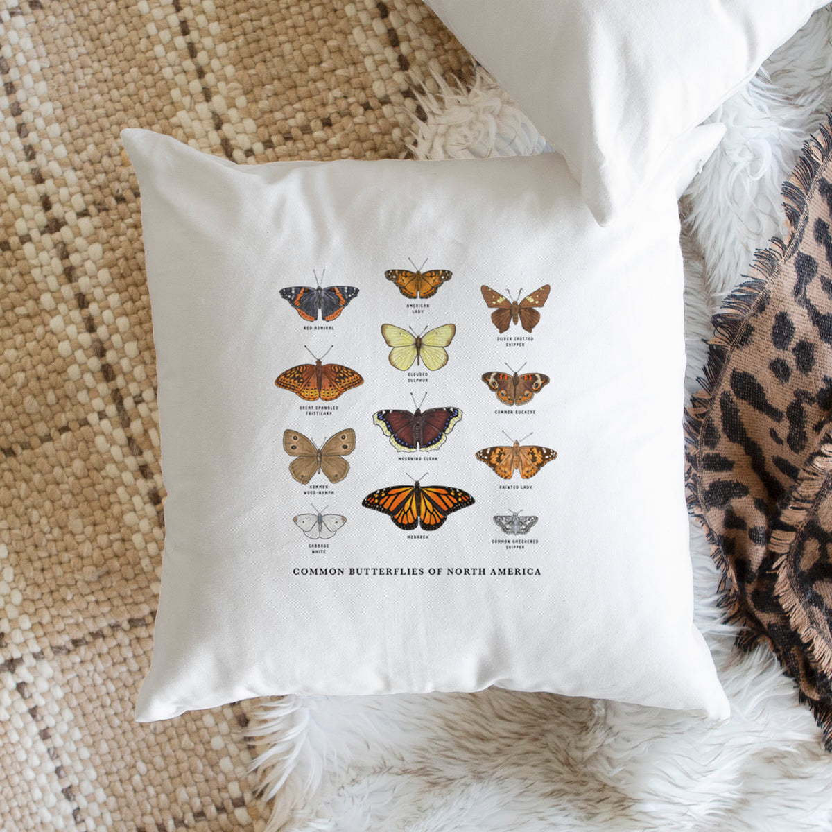 White pillow cover printed with a full-color chart of common butterflies of North America, each labeled with its species, on a woven chair.