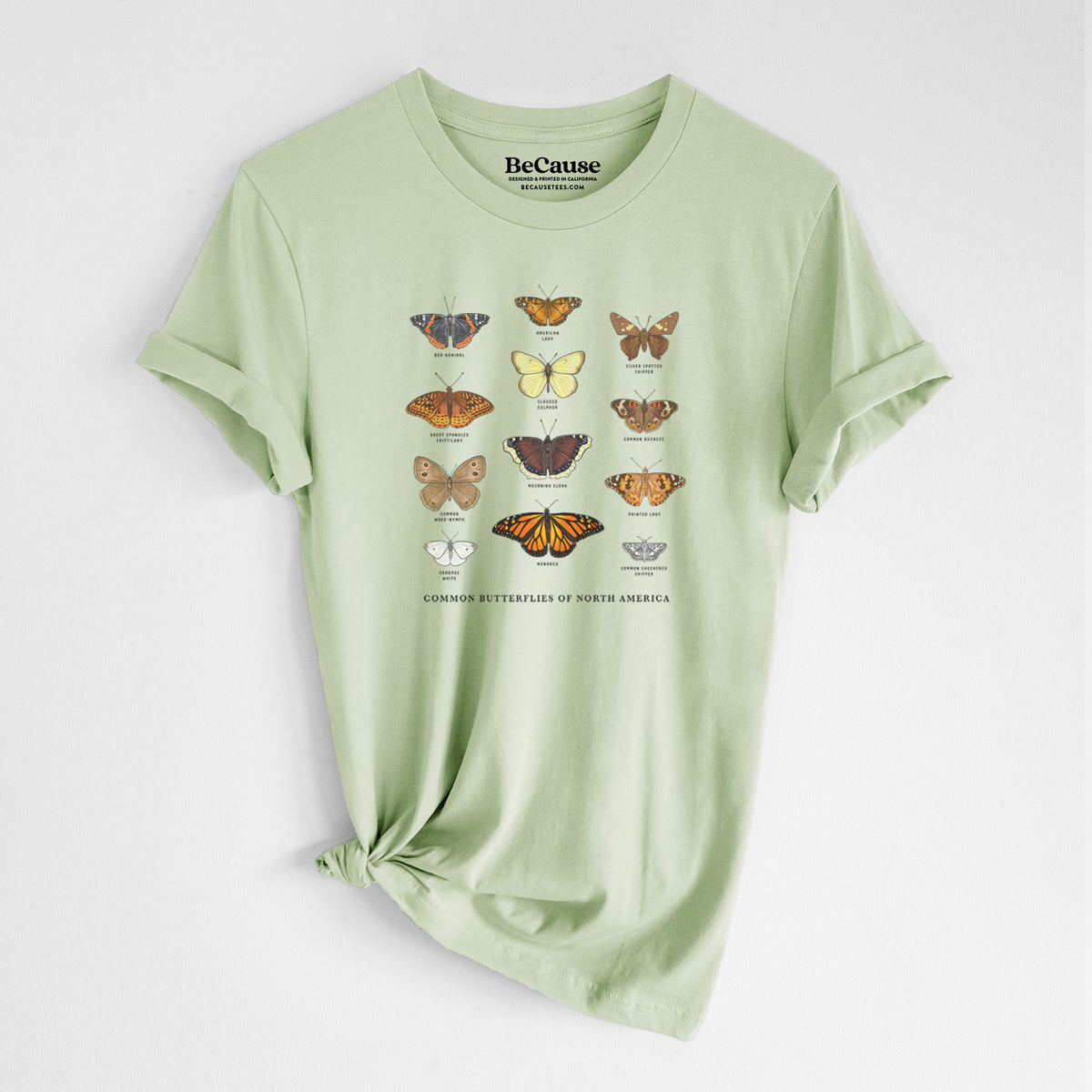 Spring green lightweight cotton t-shirt laid flat with the sleeves rolled, printed with a full-color chart of common butterflies of North America, each labeled with its species.
