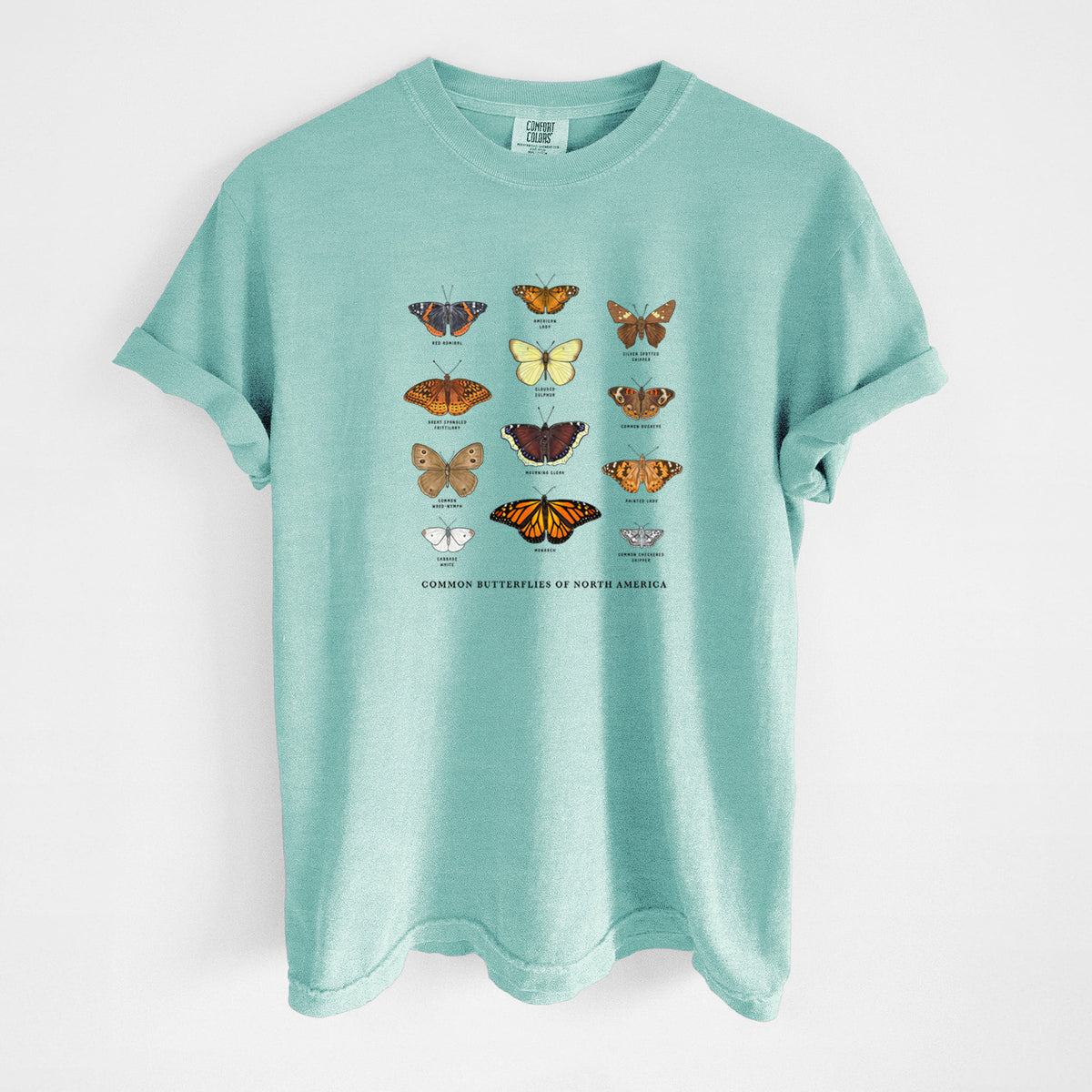 Chalky mint Comfort Colors t-shirt laid flat, printed with a full-color chart of common butterflies of North America, each labeled with its species.
