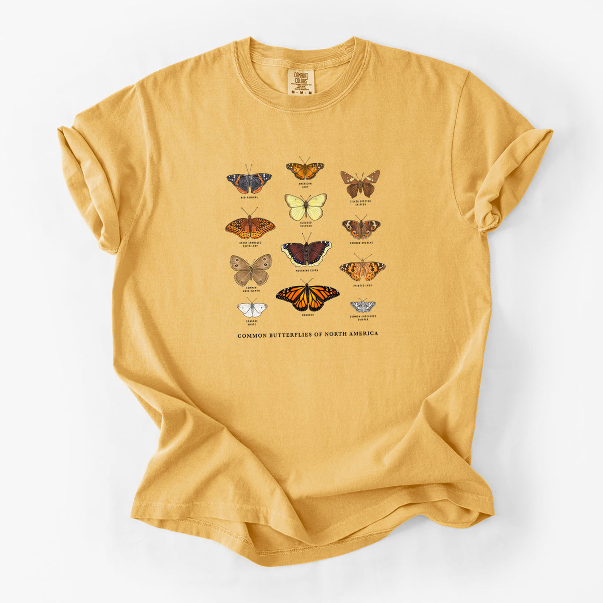 Golden wheat yellow Comfort Colors t-shirt laid flat, printed with a full-color chart of common butterflies of North America, each labeled with its species.