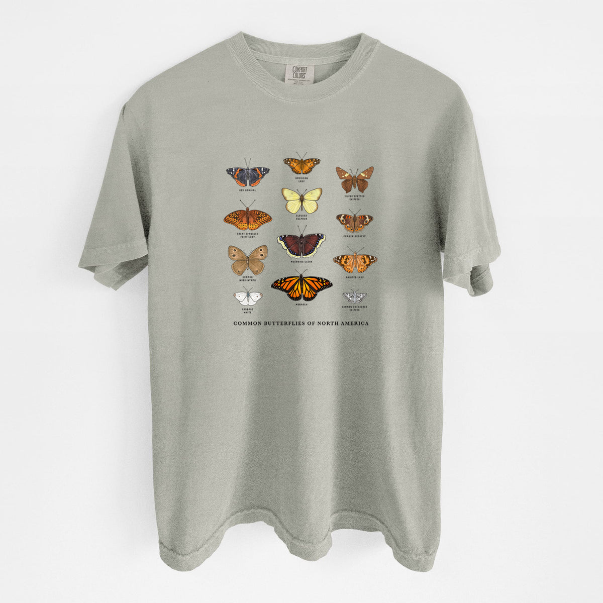 Sandstone beige Comfort Colors t-shirt laid flat, printed with a full-color chart of common butterflies of North America, each labeled with its species.