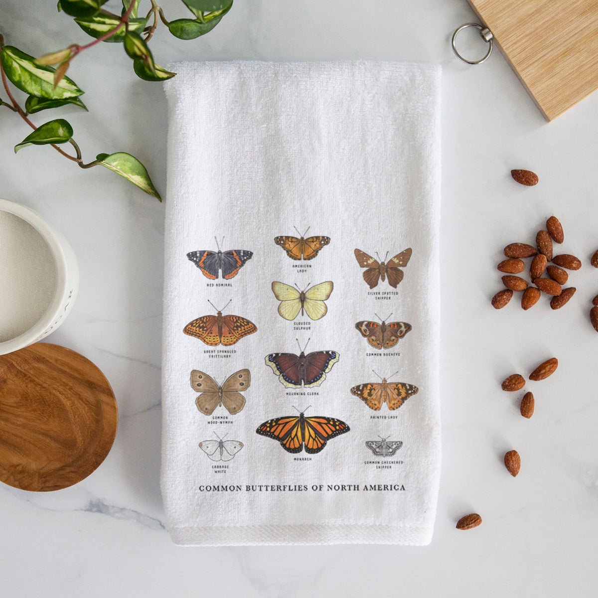 White hand towel printed with a full-color chart of common butterflies of North America, each labeled with its species.