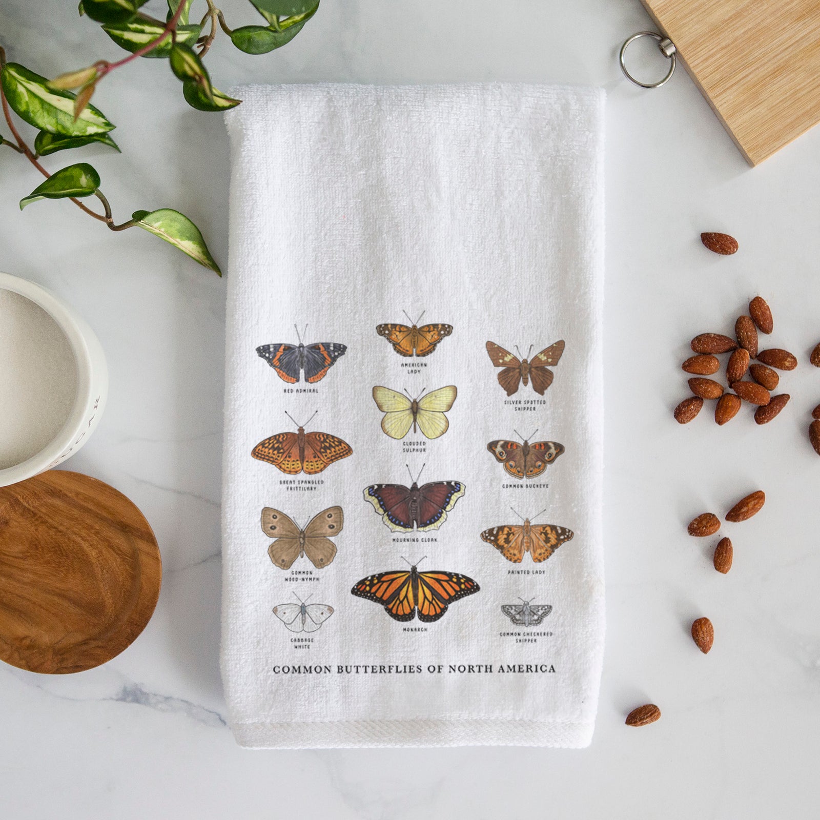White hand towel printed with a full-color chart of common butterflies of North America, each labeled with its species.