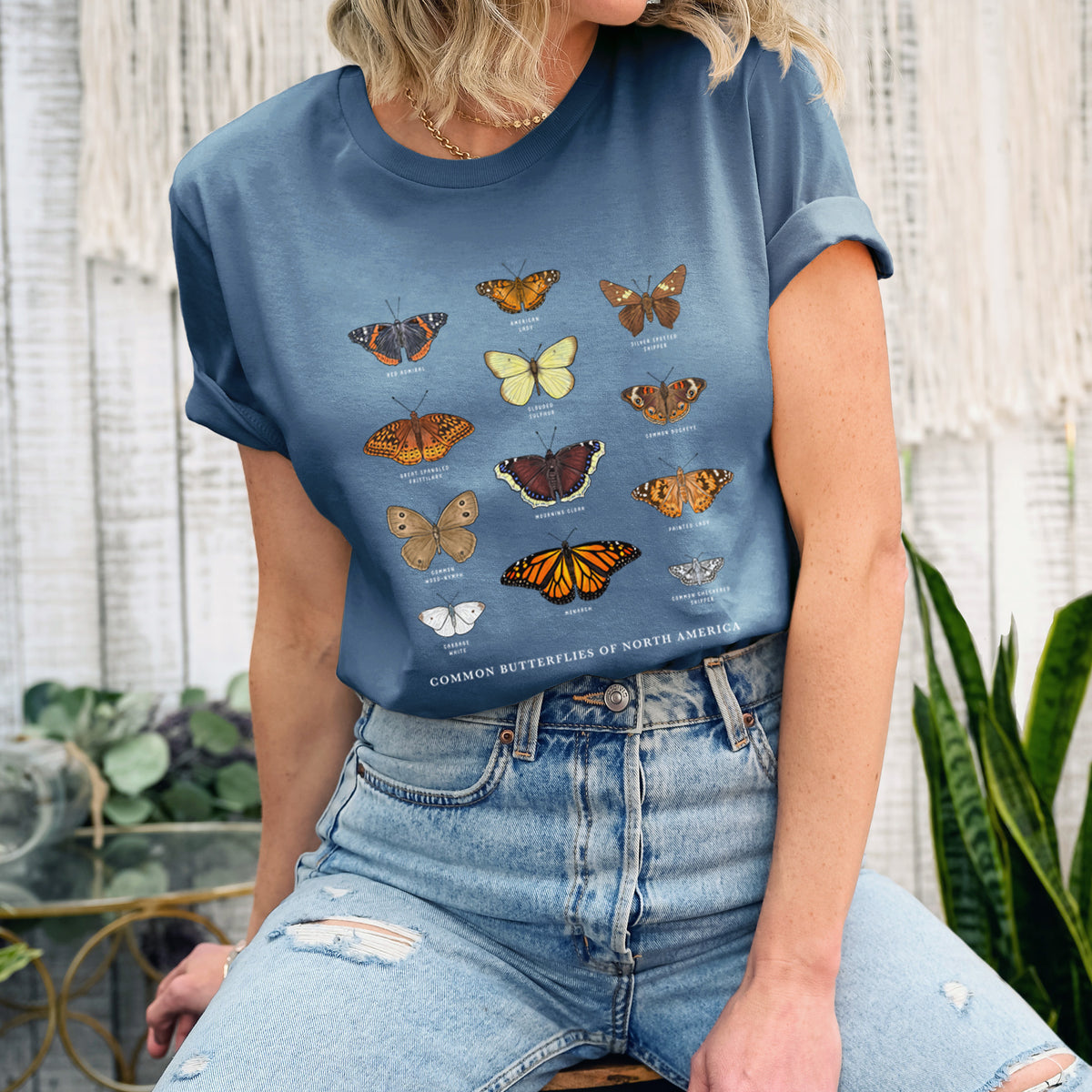 Woman wearing a steel blue lightweight cotton t-shirt printed with a full-color chart of common butterflies of North America, each labeled with its species.