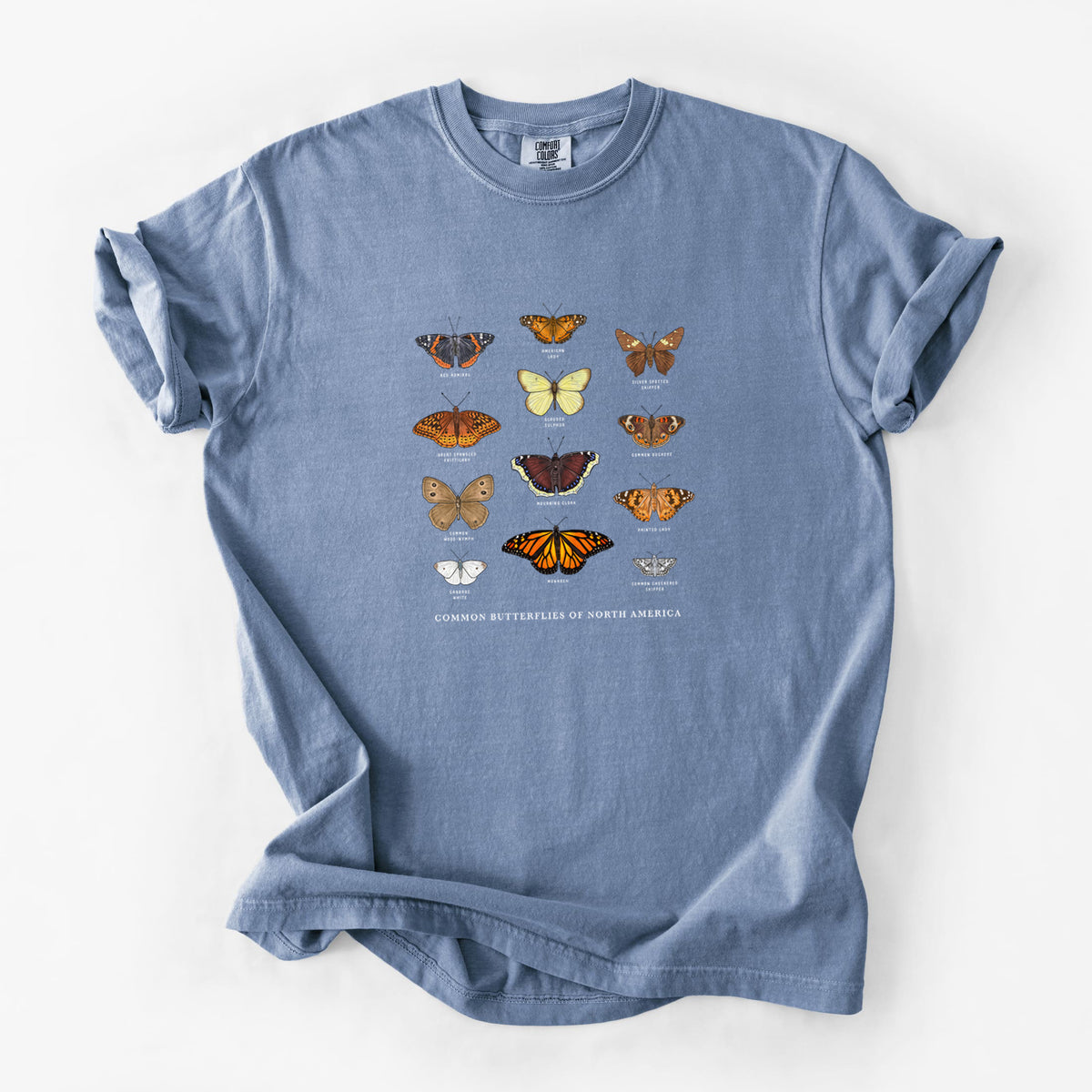 Blue jean Comfort Colors t-shirt laid flat, printed with a full-color chart of common butterflies of North America, each labeled with its species.