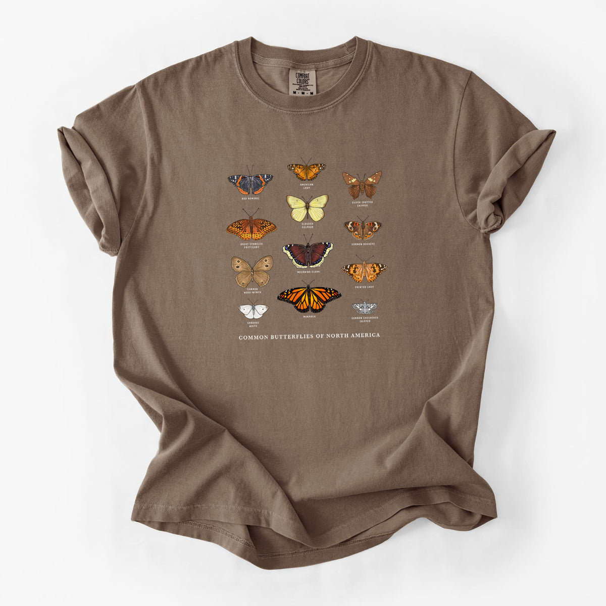Espresso brown Comfort Colors t-shirt laid flat, printed with a full-color chart of common butterflies of North America, each labeled with its species.