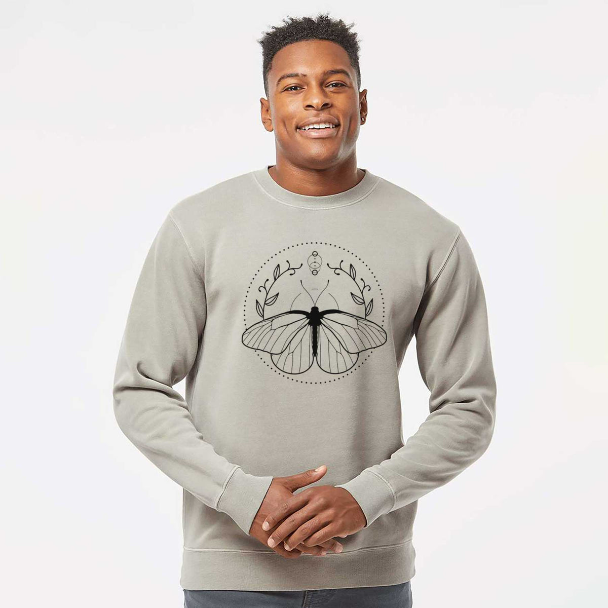 Model wearing a cement grey pigment dyed crewneck sweatshirt printed with a black ink butterfly inside a circle, framed by moon phases and leaves.