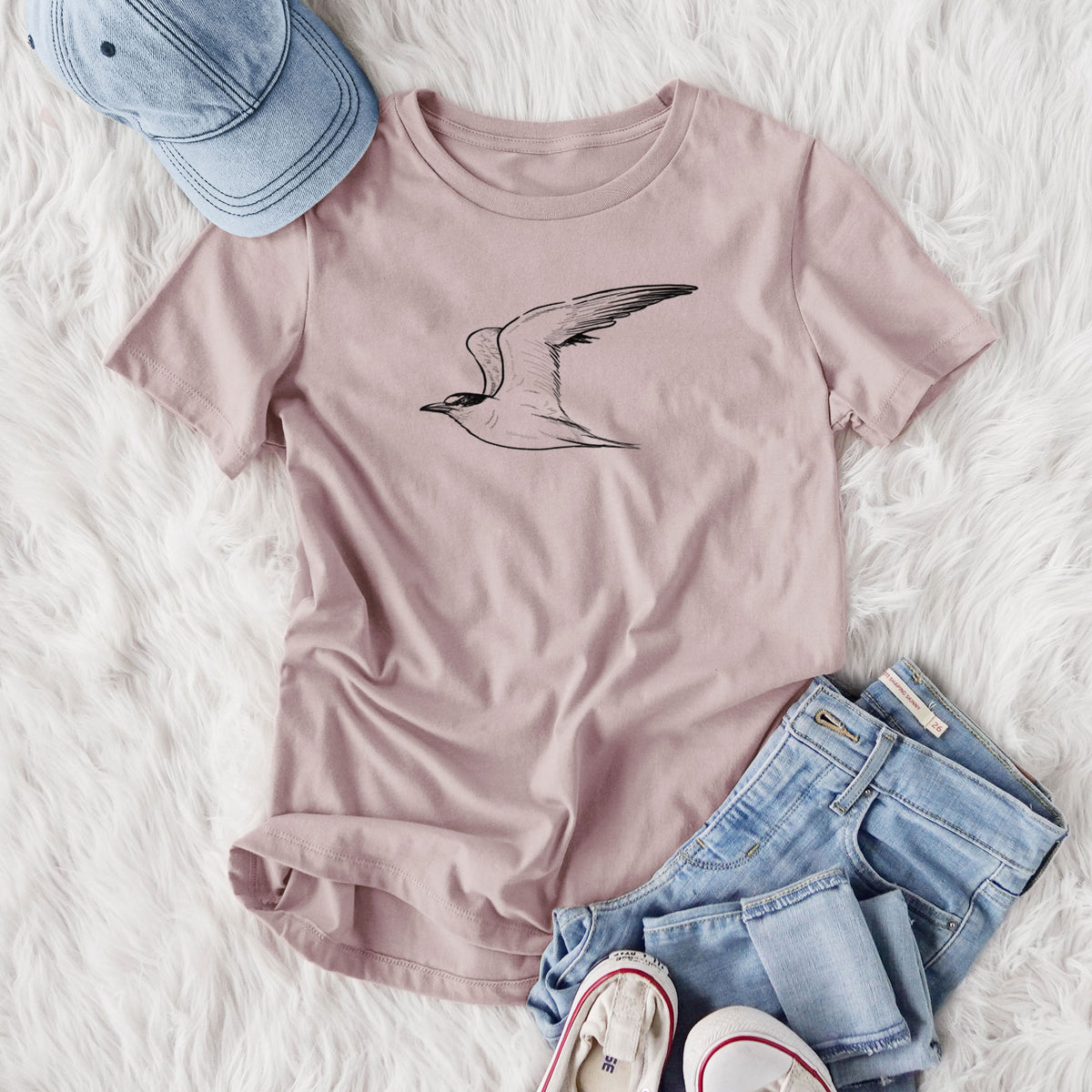 Women's relaxed fit cotton t-shirt printed with a black ink illustration of a California least tern in flight, styled flat on a white faux fur rug with jeans.