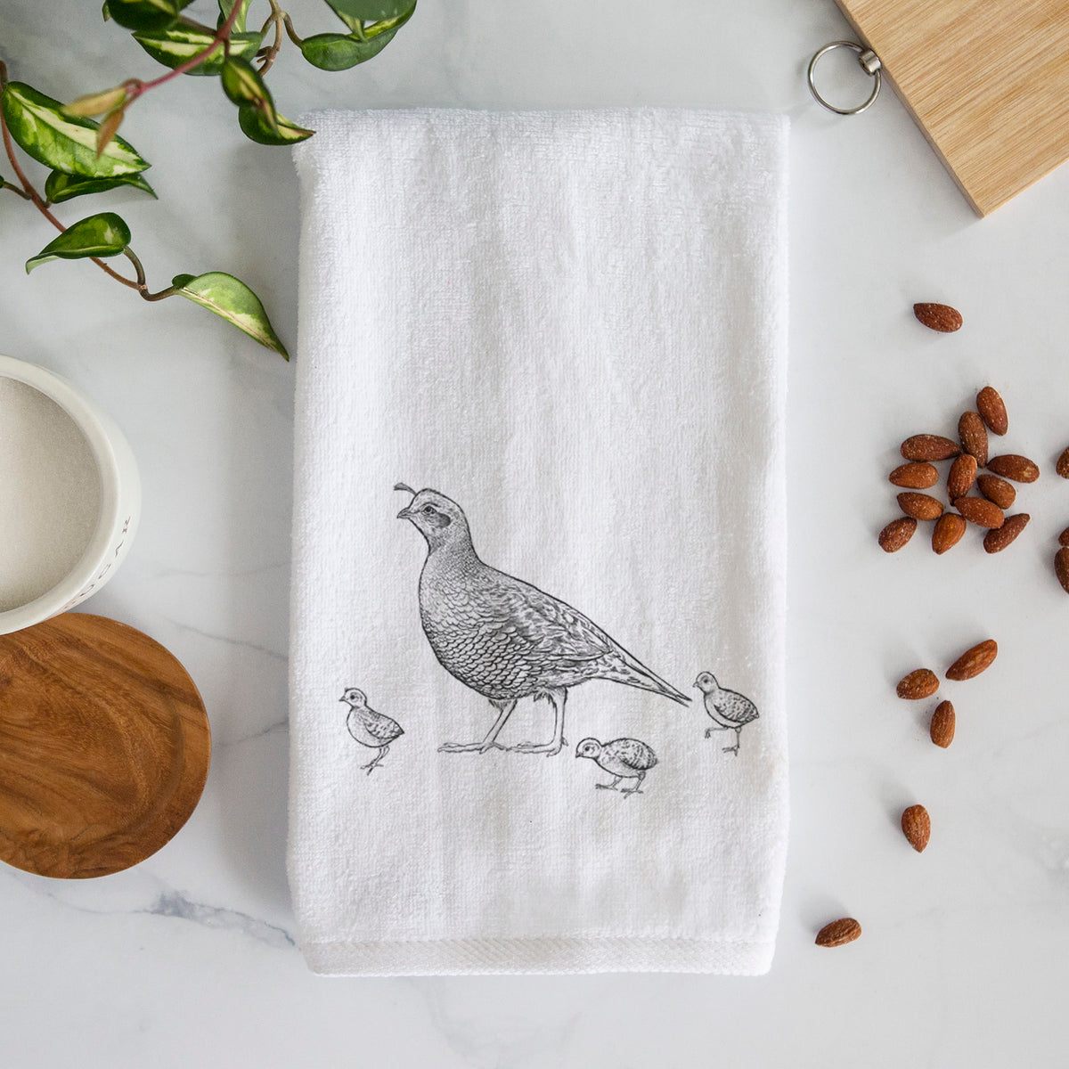 White hand towel printed with a black ink illustration of a California quail with its chicks.