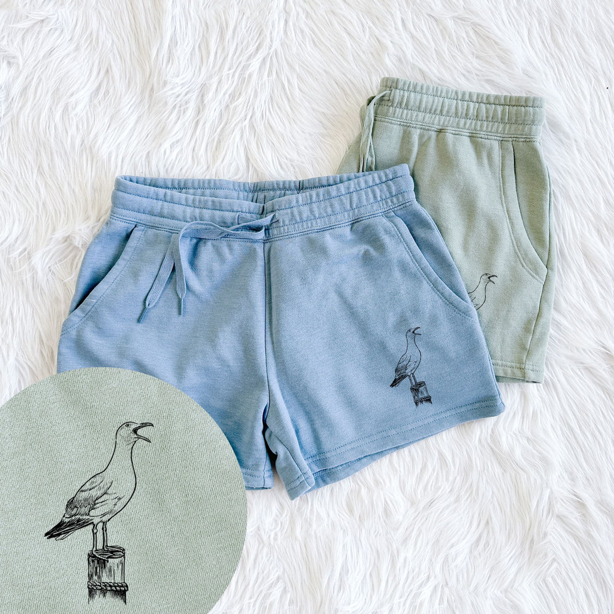 Two pairs of Cali Wave shorts in different colors printed with a black ink illustration of a California gull calling from a wooden post, with a close-up of the print.