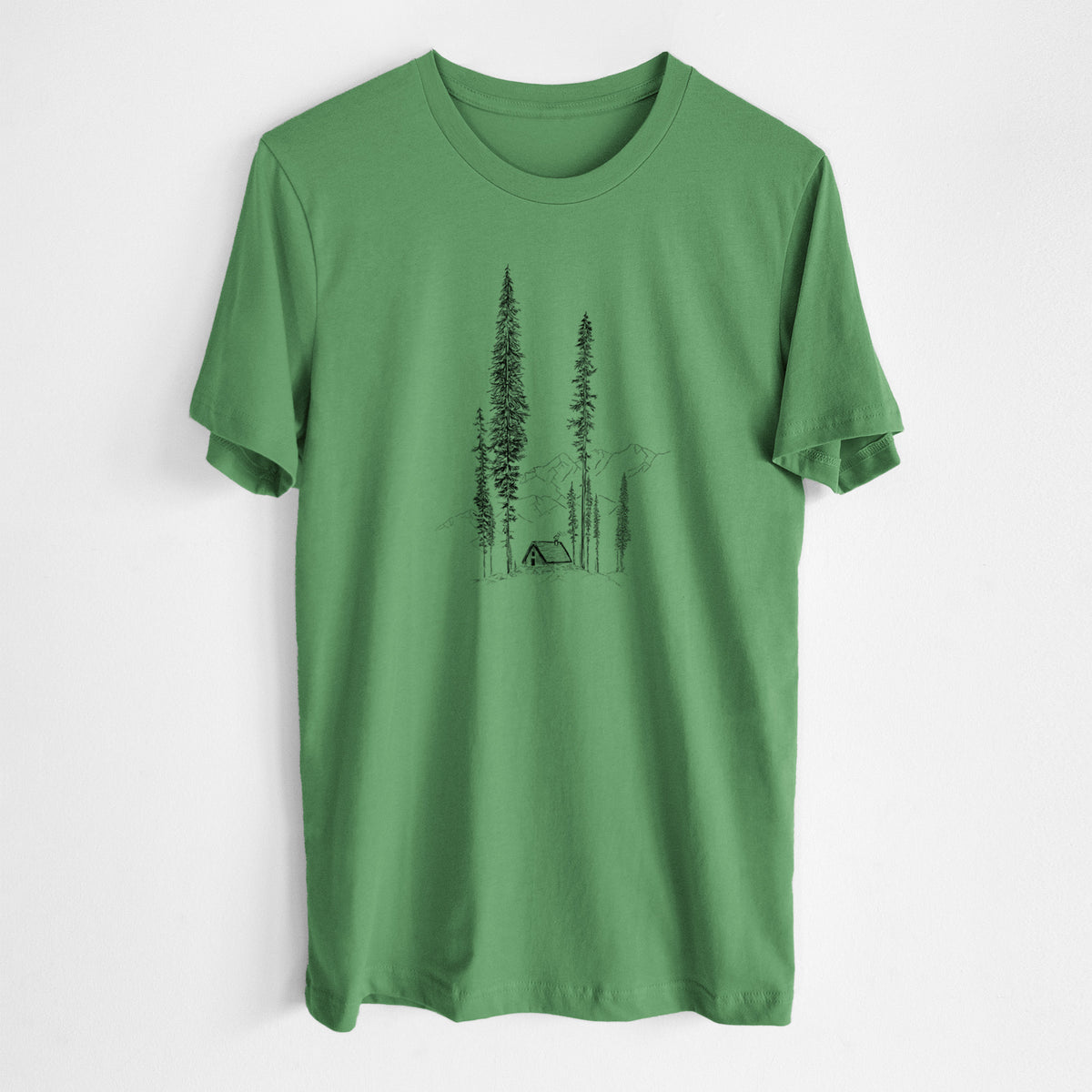 Leaf green lightweight cotton t-shirt laid flat, printed with a black ink illustration of a small cabin nestled beneath towering pine trees.