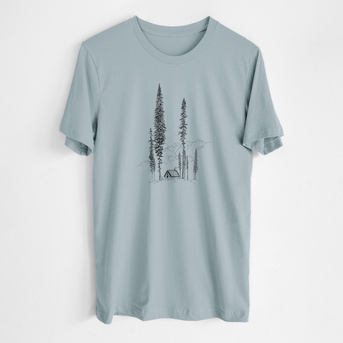 Vintage denim lightweight cotton t-shirt laid flat, printed with a black ink illustration of a small cabin nestled beneath towering pine trees.