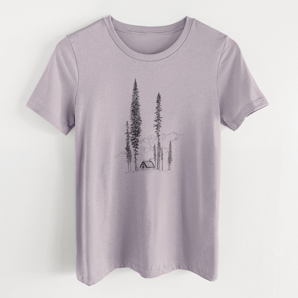 Light violet women's relaxed fit cotton t-shirt laid flat, printed with a black ink illustration of a small cabin nestled beneath towering pine trees.