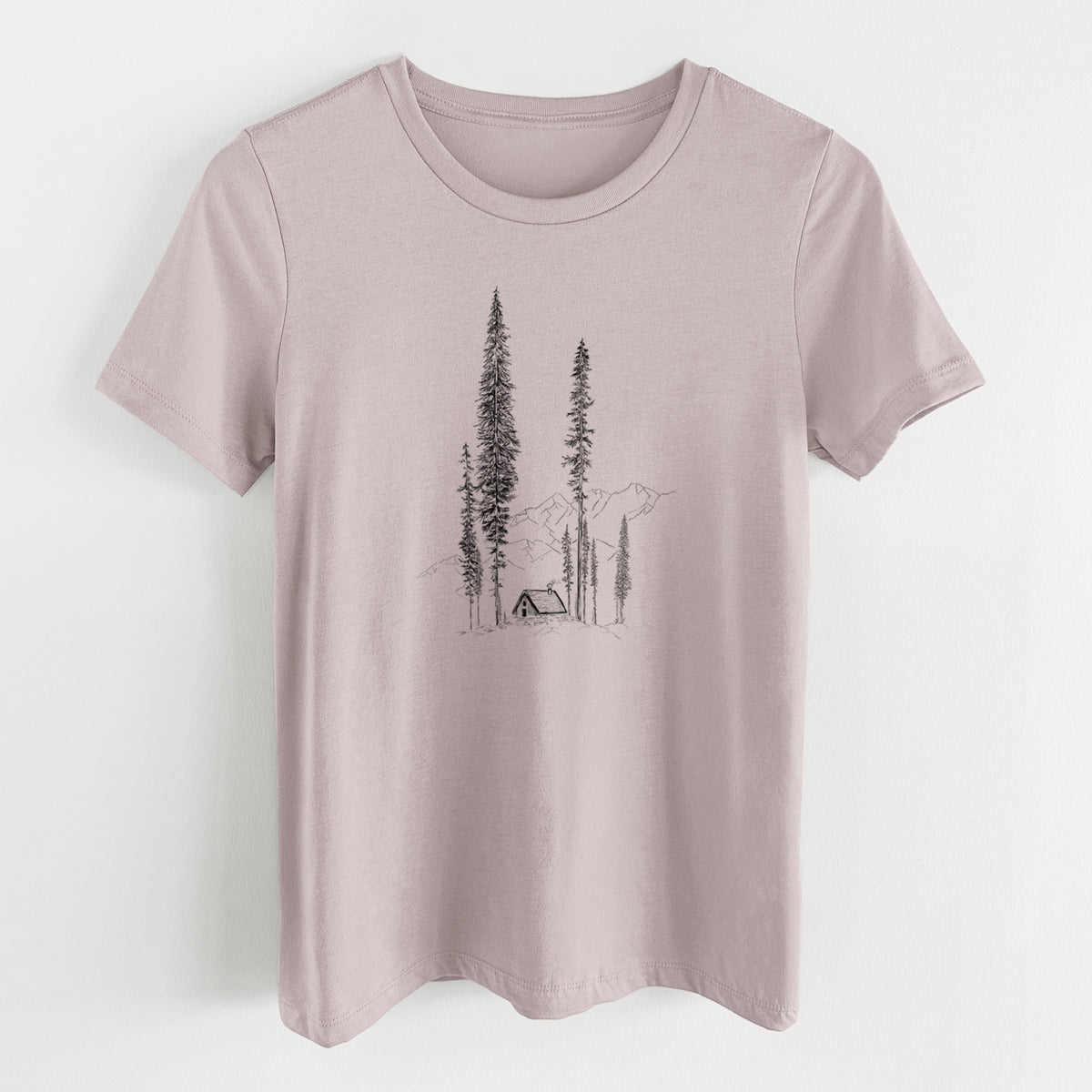 Pink gravel women's relaxed fit cotton t-shirt laid flat, printed with a black ink illustration of a small cabin nestled beneath towering pine trees.