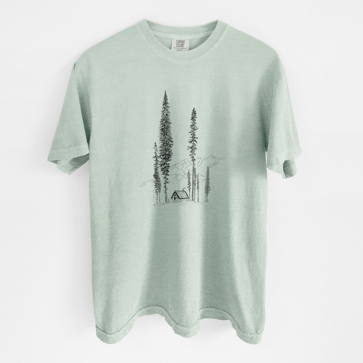 Bay green Comfort Colors t-shirt laid flat, printed with a black ink illustration of a small cabin nestled beneath towering pine trees.