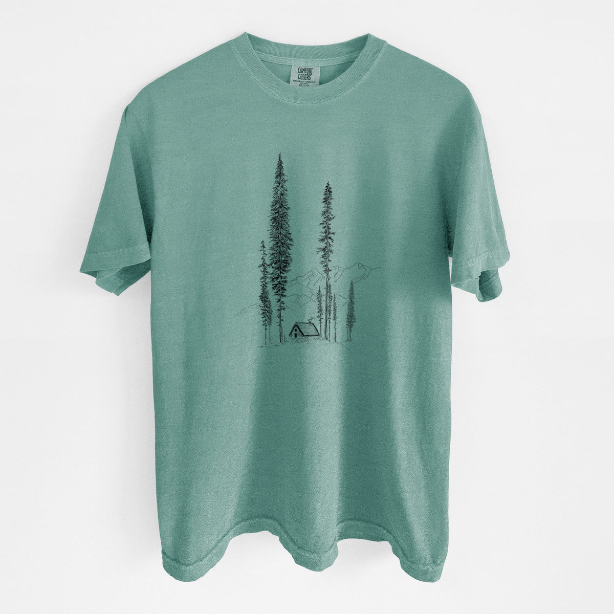 Reef green Comfort Colors t-shirt laid flat, printed with a black ink illustration of a small cabin nestled beneath towering pine trees.