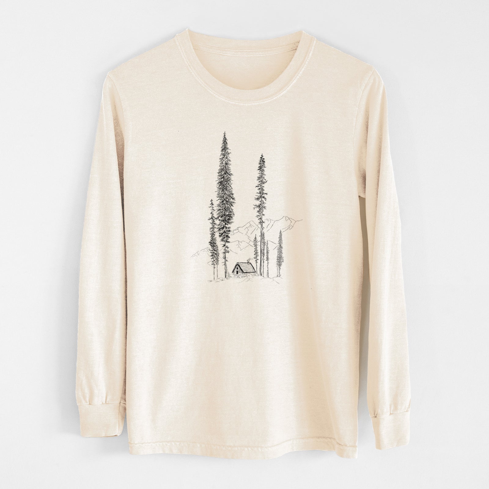 Ivory Comfort Colors long sleeve shirt laid flat, printed with a black ink illustration of a small cabin nestled beneath towering pine trees.