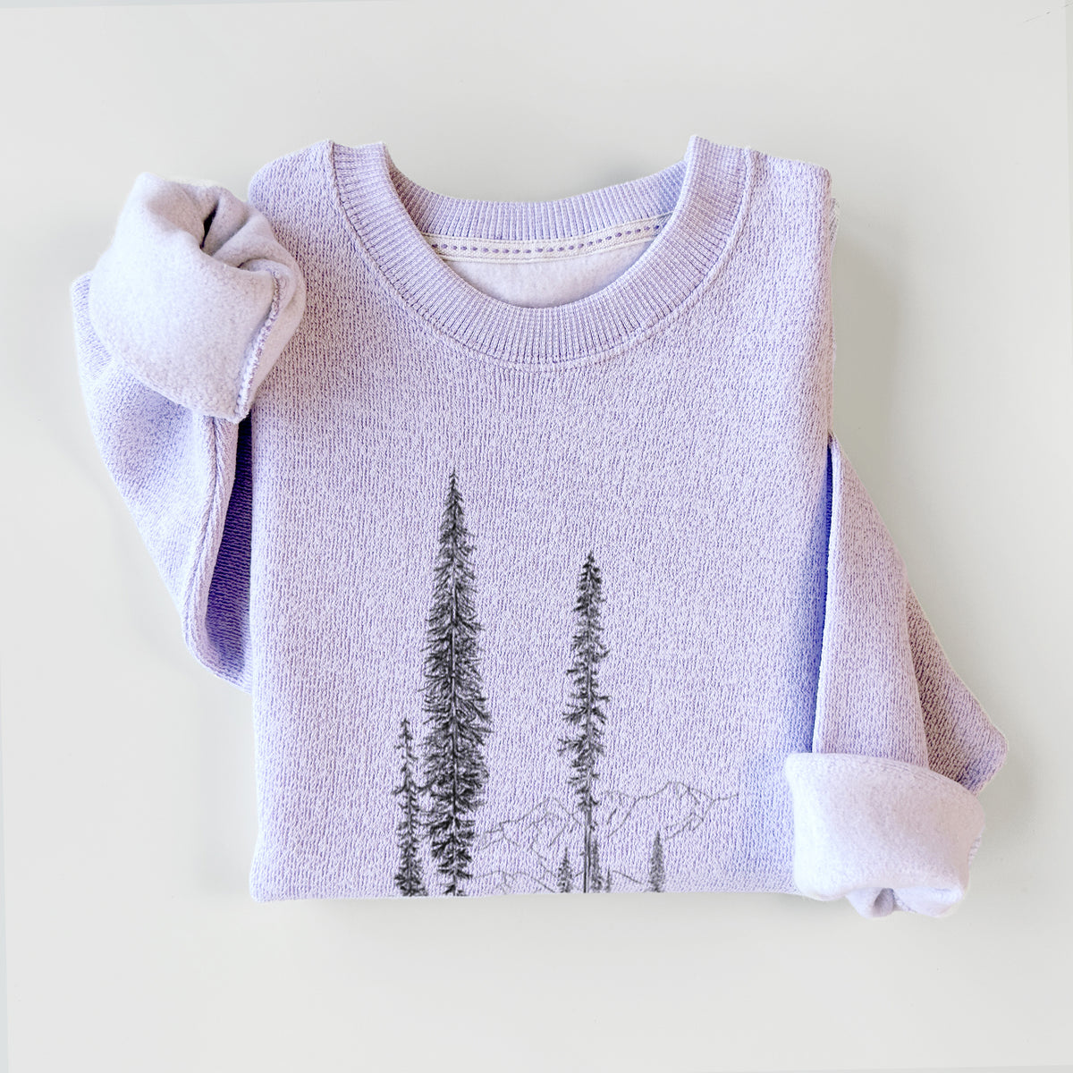 Ice purple knit sweatshirt printed with a black ink illustration of a small cabin nestled beneath towering pine trees, styled flat.