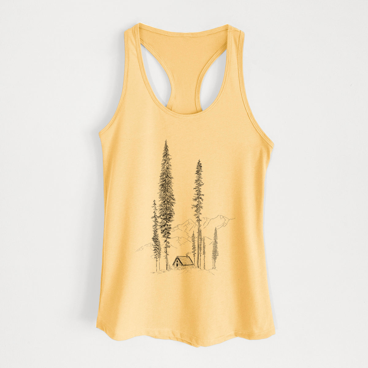 Banana cream women's racerback tank top laid flat, printed with a black ink illustration of a small cabin nestled beneath towering pine trees.