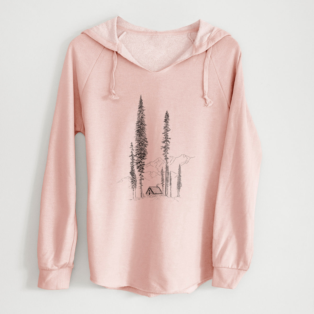 Blush pink women's Cali Wave hooded sweatshirt laid flat, printed with a black ink illustration of a small cabin nestled beneath towering pine trees.