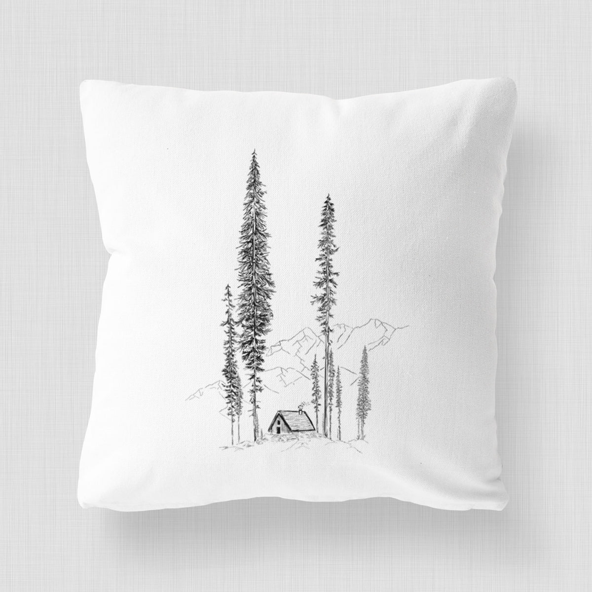 White pillow cover printed with a black ink illustration of a small cabin nestled beneath towering pine trees.