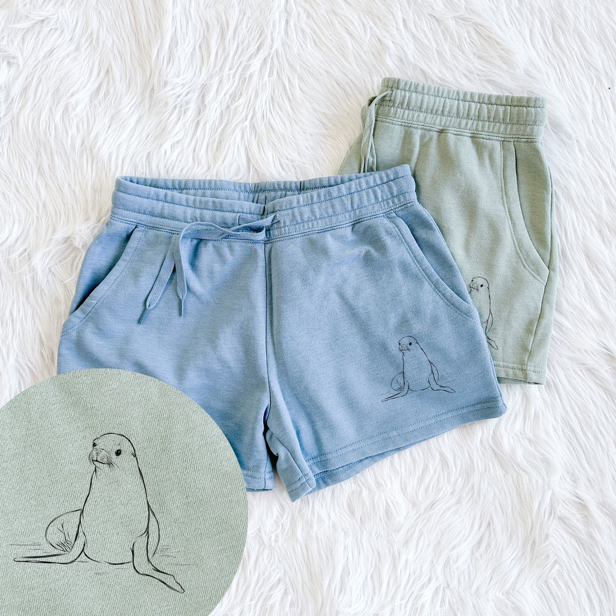 Two pairs of Cali Wave shorts in different colors printed with a black ink illustration of a California sea lion sitting upright, with a close-up of the print.