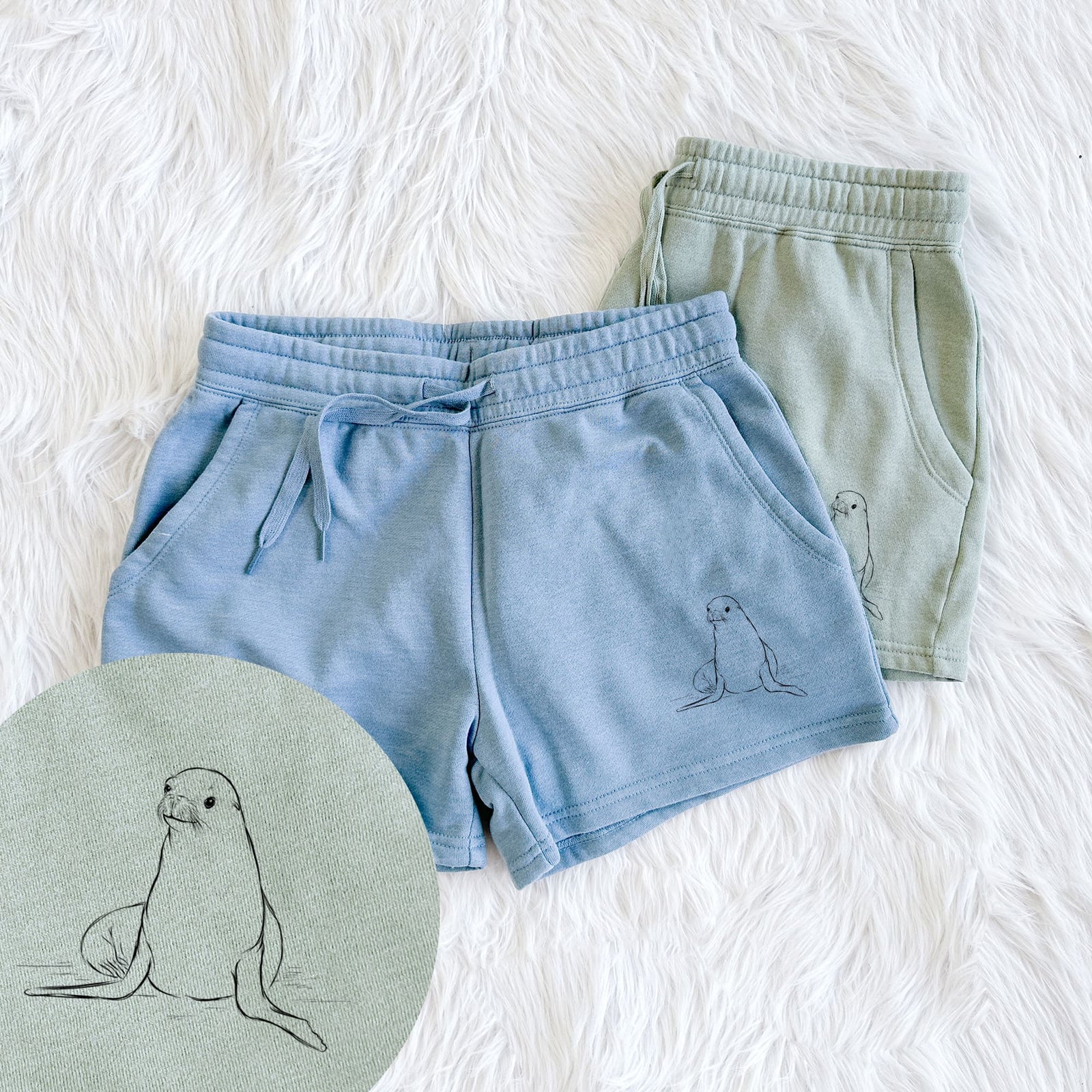 Two pairs of Cali Wave shorts in different colors printed with a black ink illustration of a California sea lion sitting upright, with a close-up of the print.