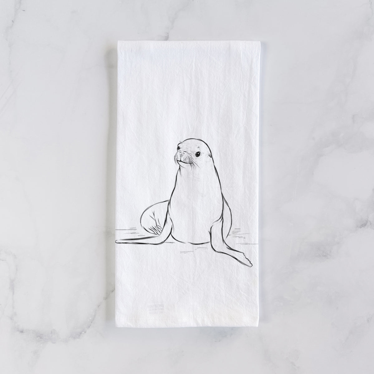White cotton tea towel laid flat on marble, printed with a black ink illustration of a California sea lion sitting upright.