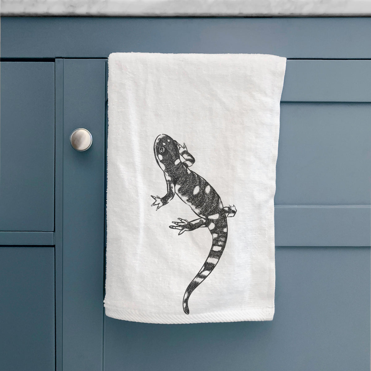 White hand towel printed with a detailed black ink illustration of a spotted California tiger salamander, hanging on a cabinet door.
