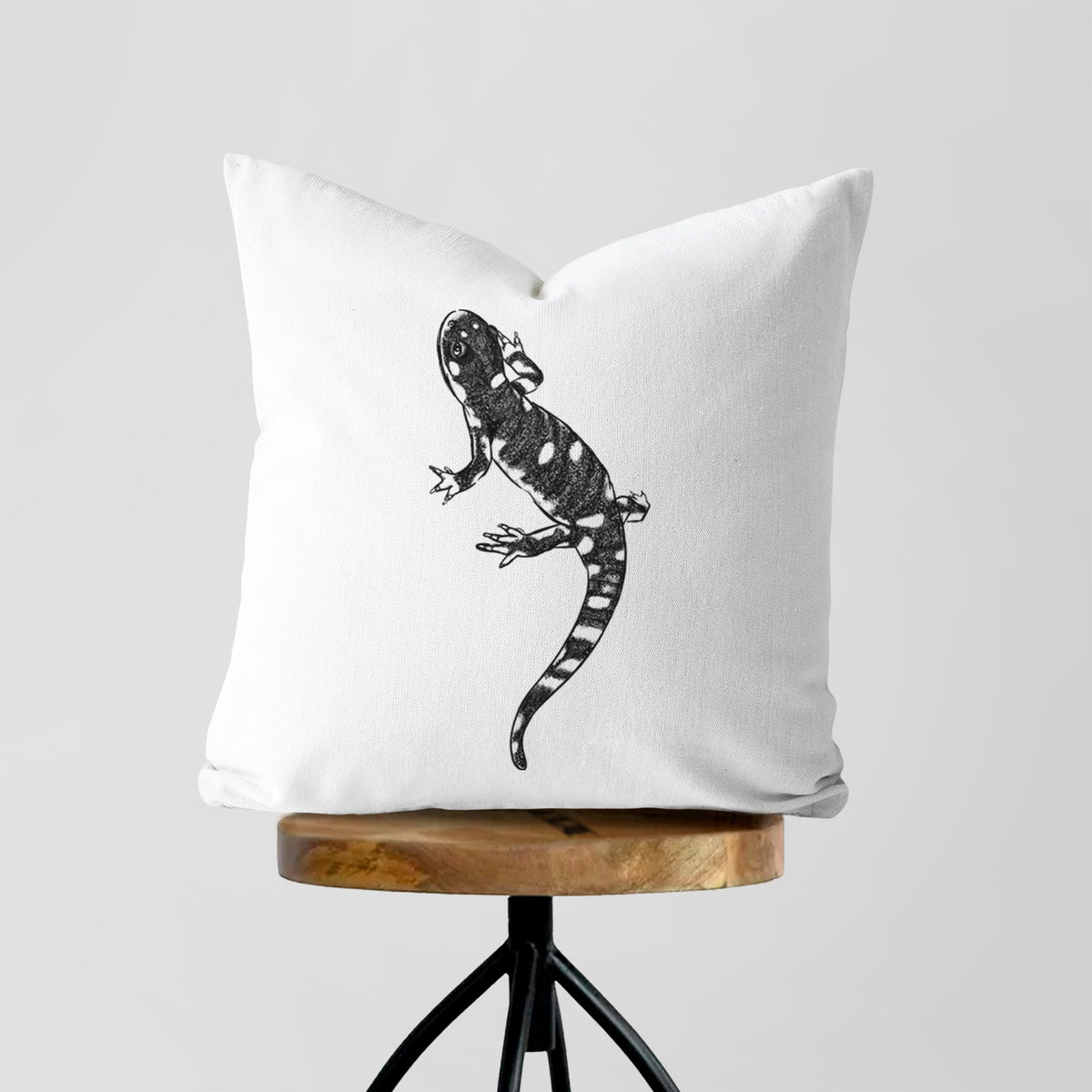 White pillow cover printed with a detailed black ink illustration of a spotted California tiger salamander, on a wooden stool.