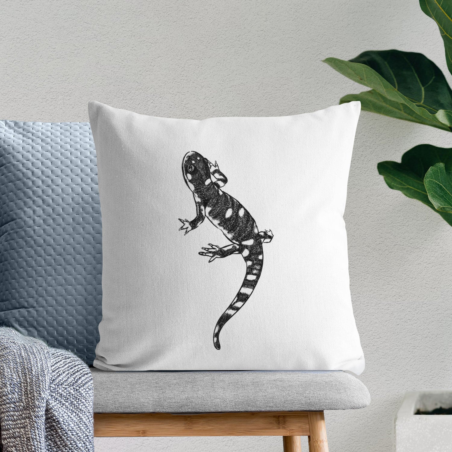 White pillow cover printed with a detailed black ink illustration of a spotted California tiger salamander, on a bench beside plants.