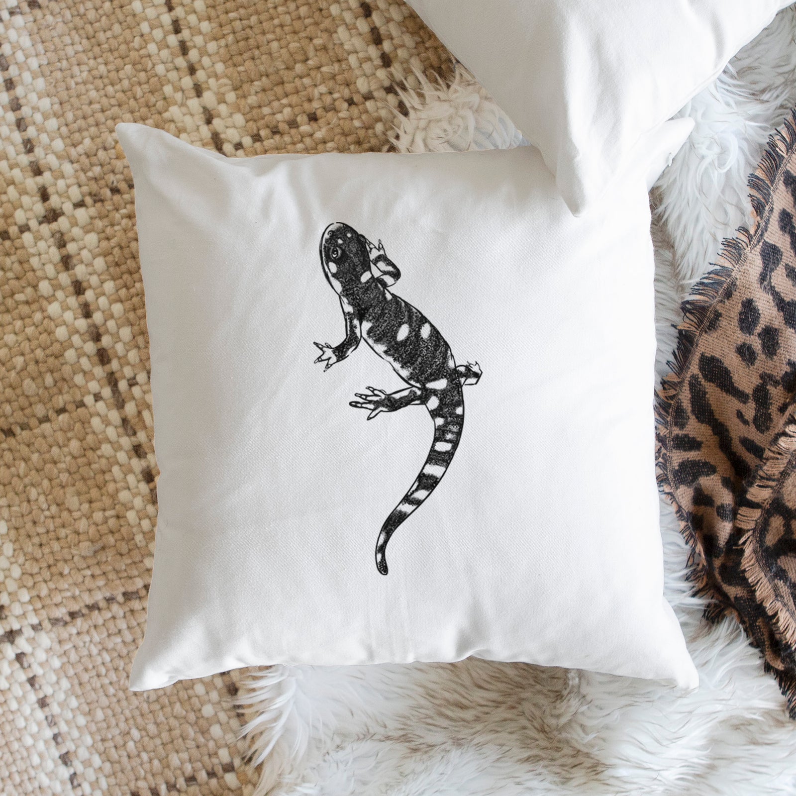 White pillow cover printed with a detailed black ink illustration of a spotted California tiger salamander, on a bench beside plants.