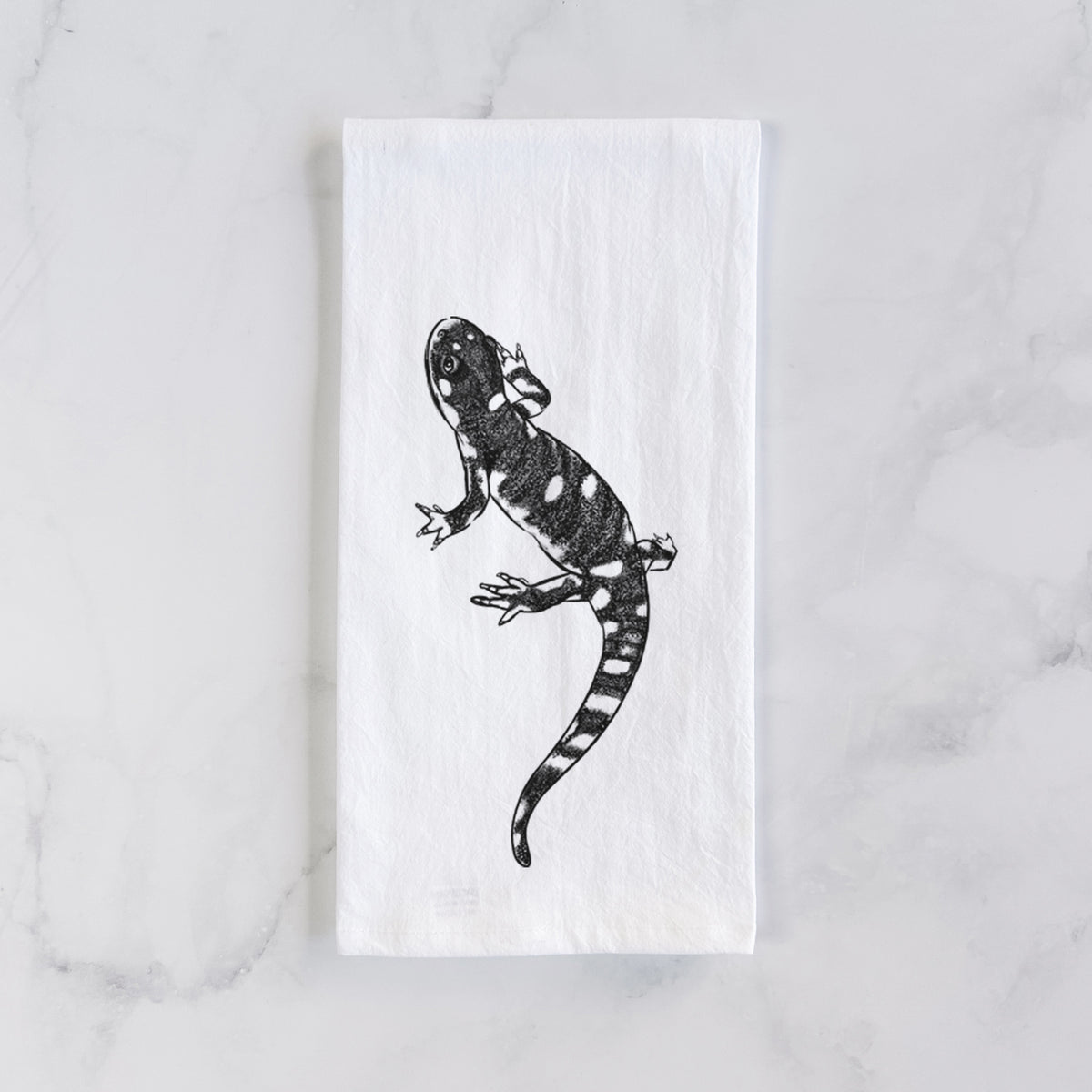 White cotton tea towel laid flat on marble, printed with a detailed black ink illustration of a spotted California tiger salamander.