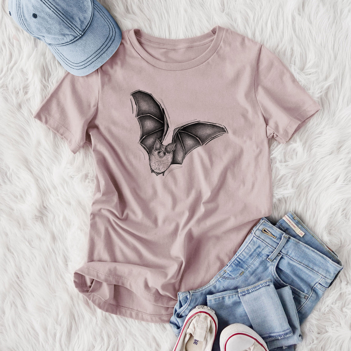 Women's relaxed fit cotton t-shirt printed with a detailed black ink illustration of a California leaf-nosed bat in flight, styled flat on a white faux fur rug with jeans.