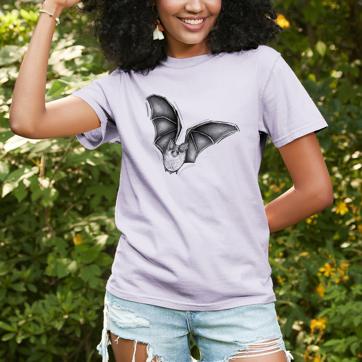Woman wearing a Comfort Colors t-shirt printed with a detailed black ink illustration of a California leaf-nosed bat in flight, outdoors.