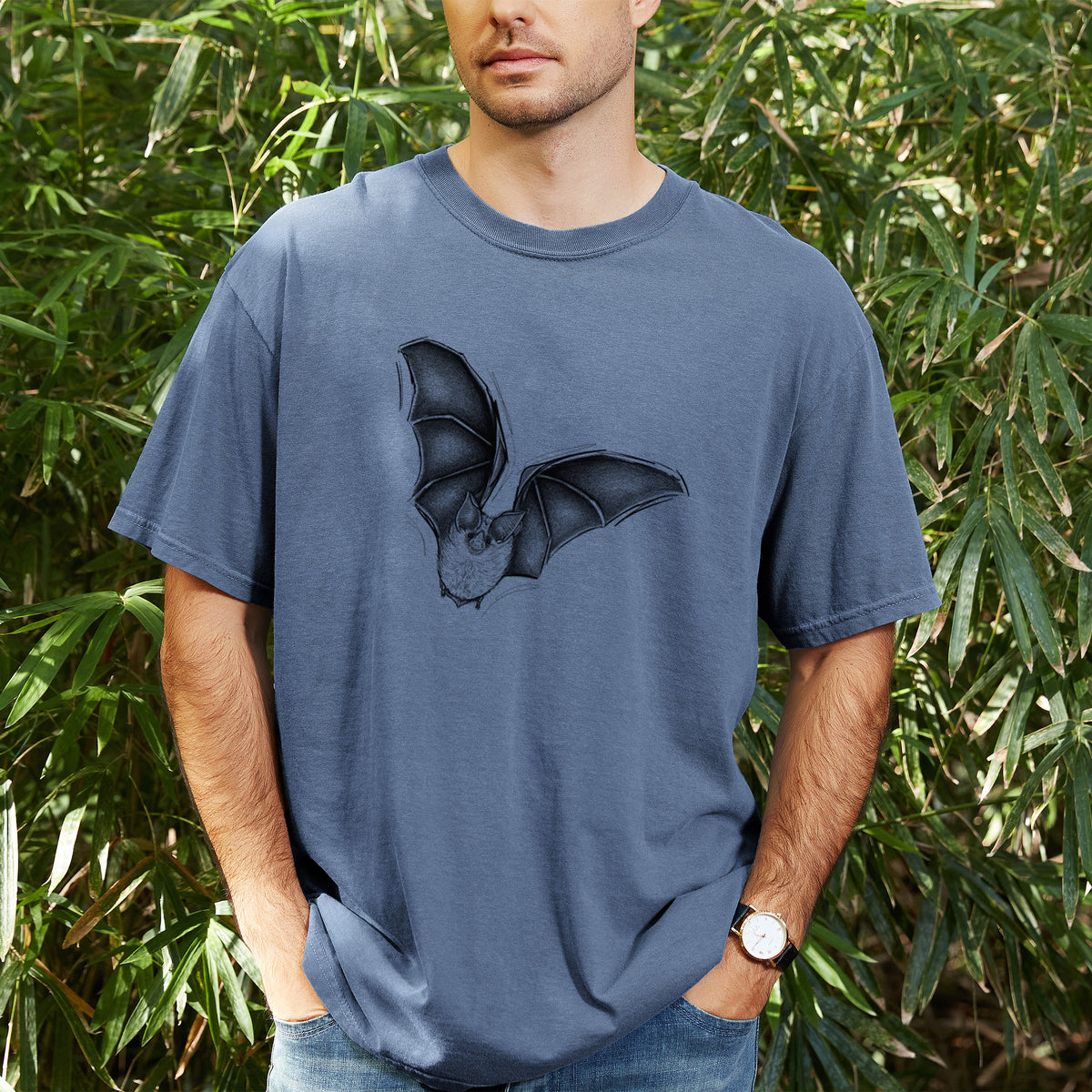 Man wearing a Comfort Colors t-shirt printed with a detailed black ink illustration of a California leaf-nosed bat in flight, outdoors.