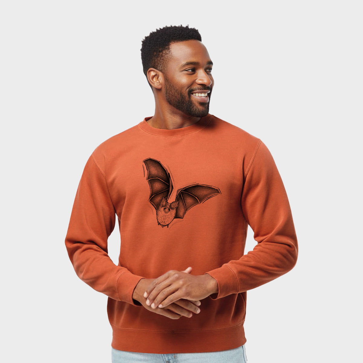 Model wearing an amber orange pigment dyed crewneck sweatshirt printed with a detailed black ink illustration of a California leaf-nosed bat in flight.