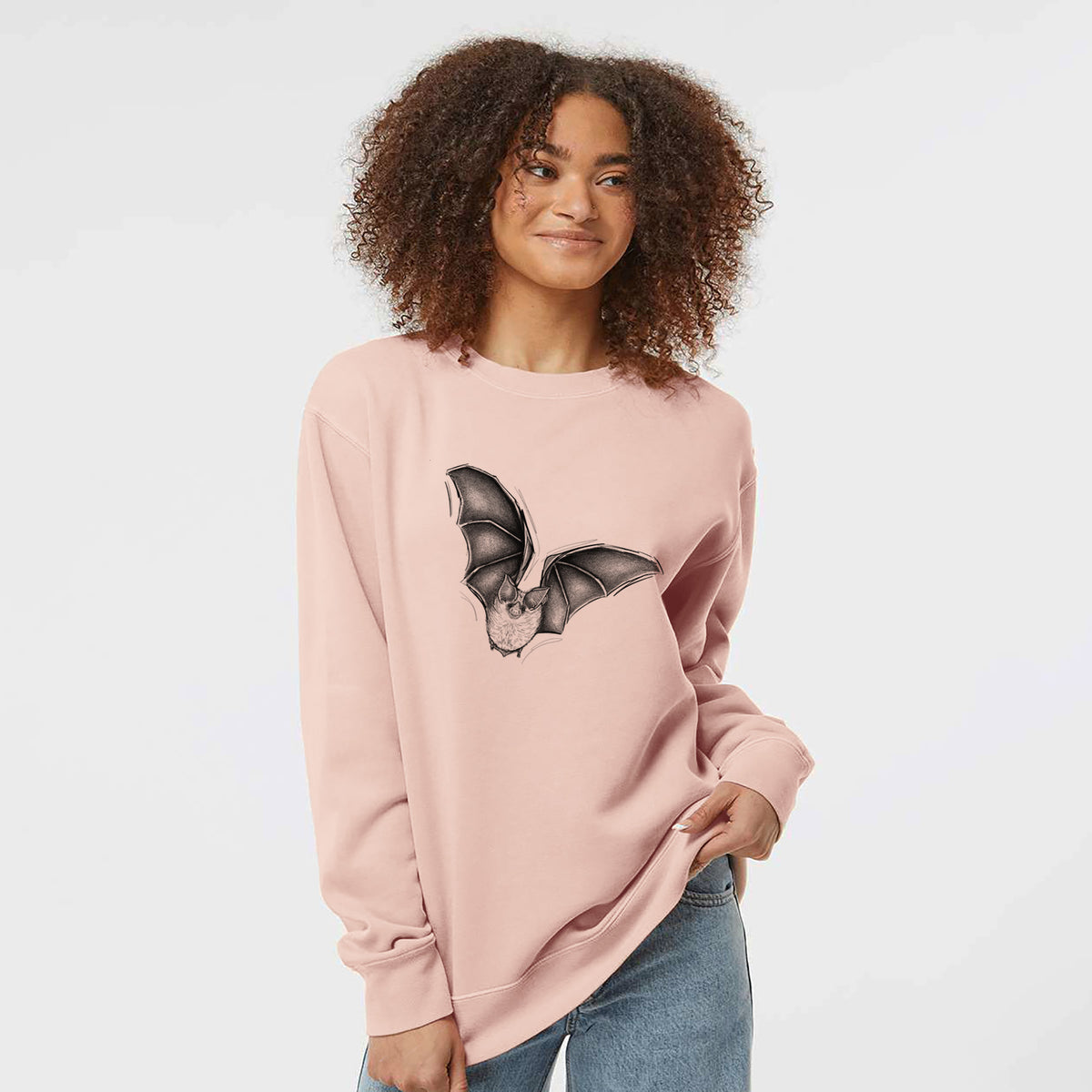Model wearing a dusty pink pigment dyed crewneck sweatshirt printed with a detailed black ink illustration of a California leaf-nosed bat in flight.