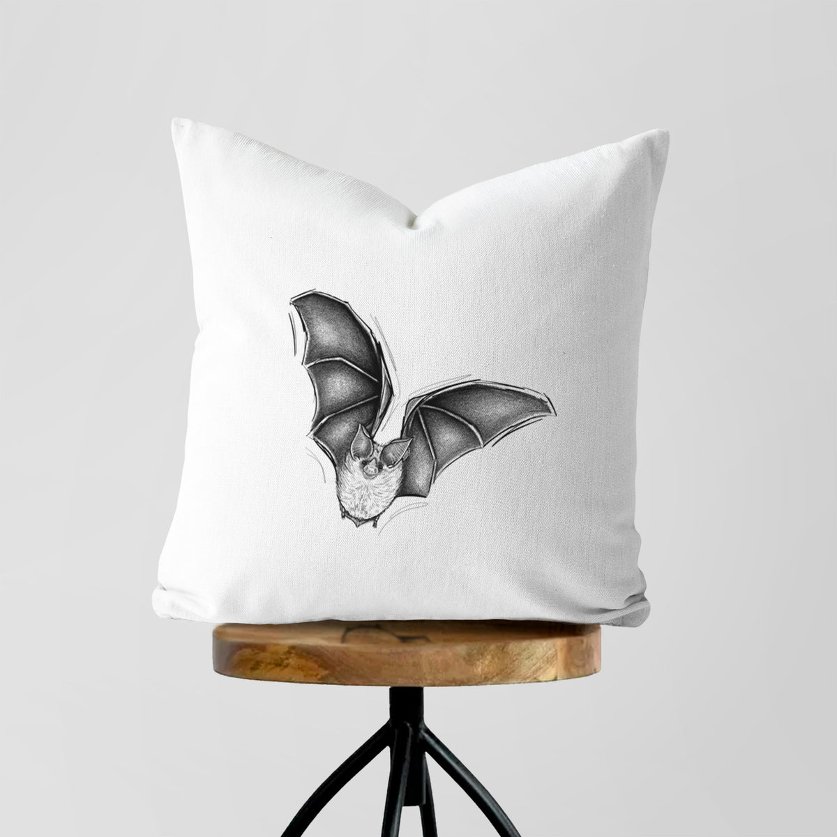 White pillow cover printed with a detailed black ink illustration of a California leaf-nosed bat in flight, on a wooden stool.