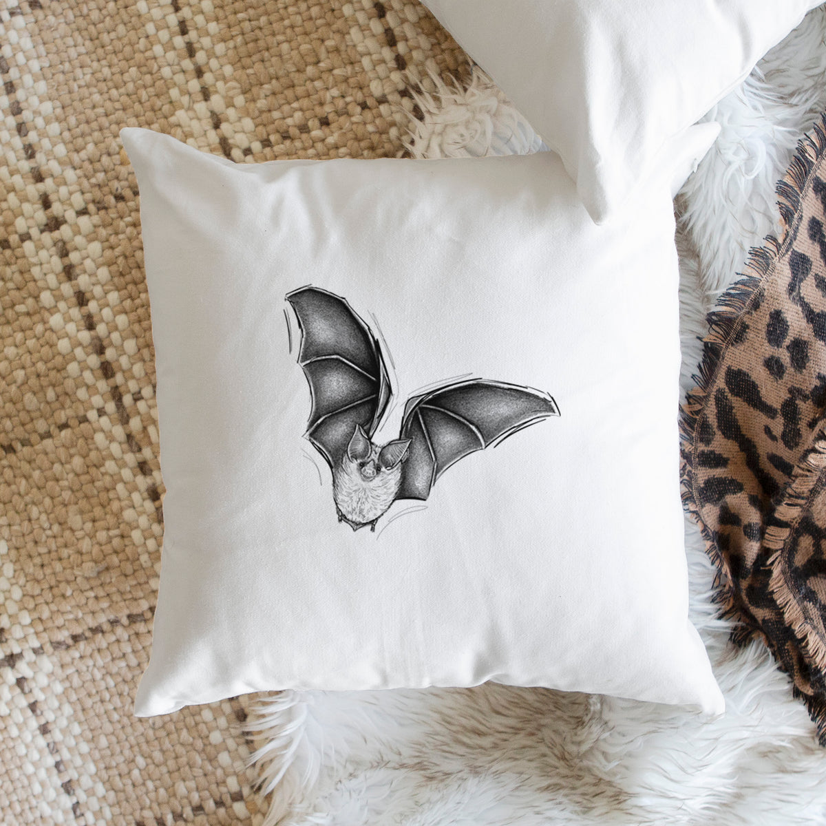 White pillow cover printed with a detailed black ink illustration of a California leaf-nosed bat in flight, on a woven chair.