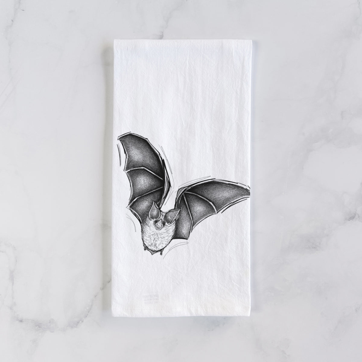 White cotton tea towel laid flat on marble, printed with a detailed black ink illustration of a California leaf-nosed bat in flight.
